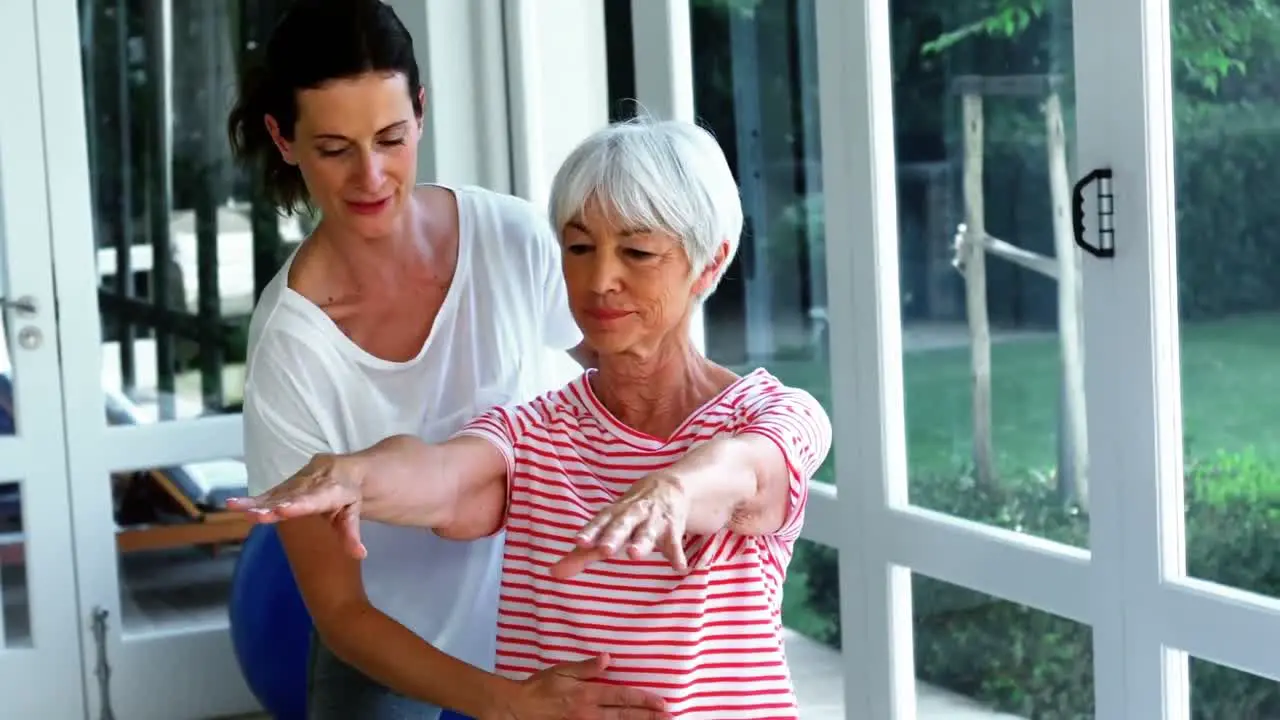 Female coach assisting senior woman in performing exercise