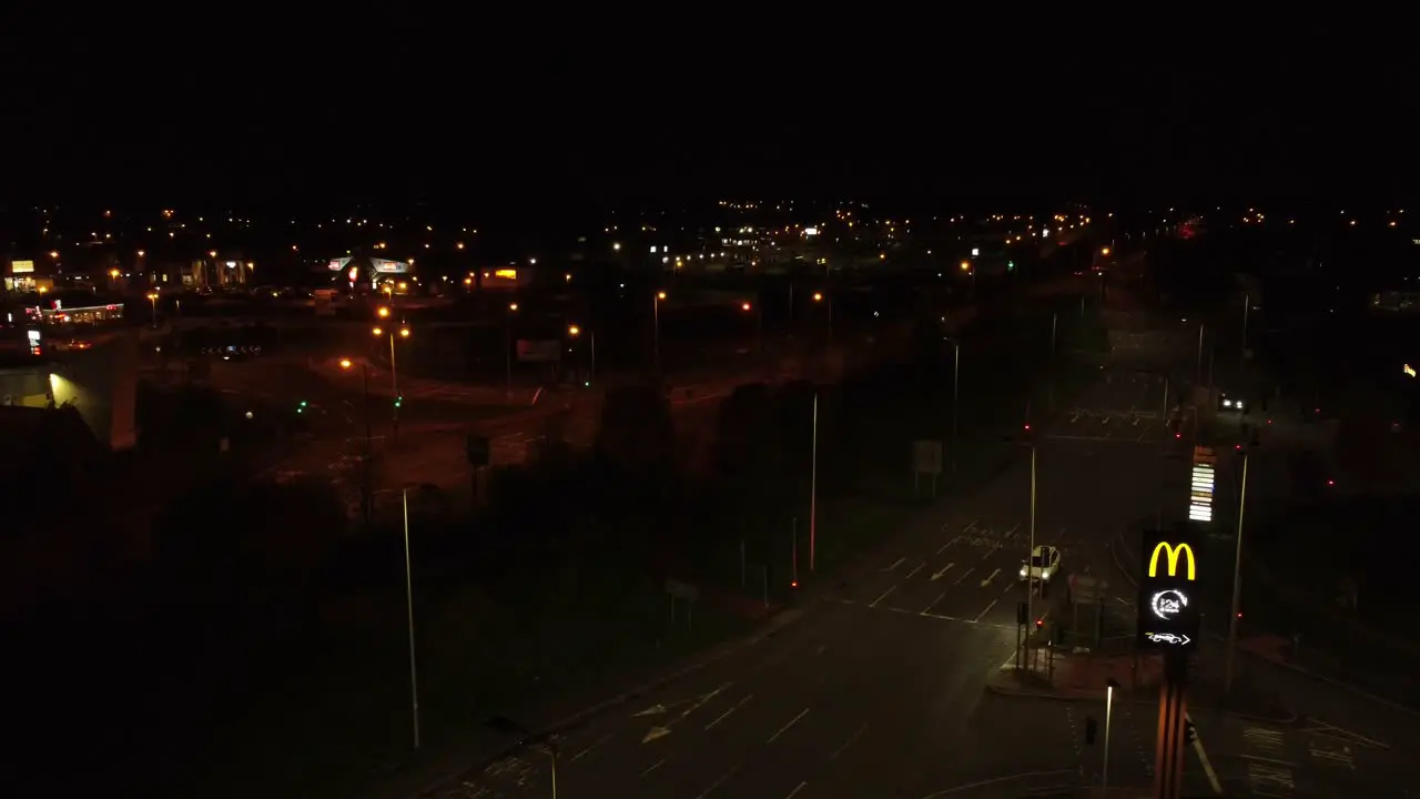 McDonalds fast food drive through logo illuminated at night next to Northern UK town highway rising aerial view right