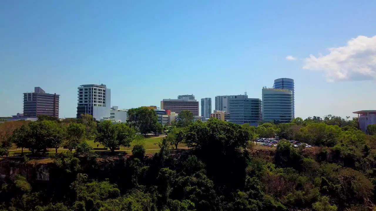 Drone footage flying up and towards Darwin city from a southerly direction over the Darwin harbour revealing Darwin city from behind the foreshore tree line