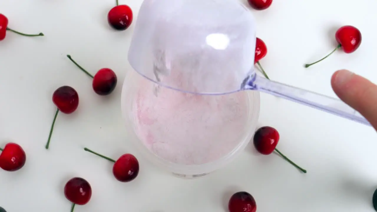 Static Birdseye shot from a shaker and spoon with tasty cherry Whey powder which is added with surrounding cherries on white base