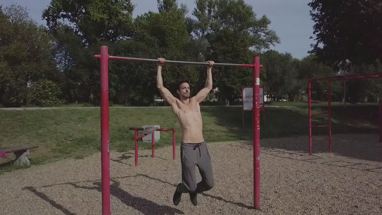 Beautiful fit young man doing pull ups in the park male athlete doing exercise and spending active time