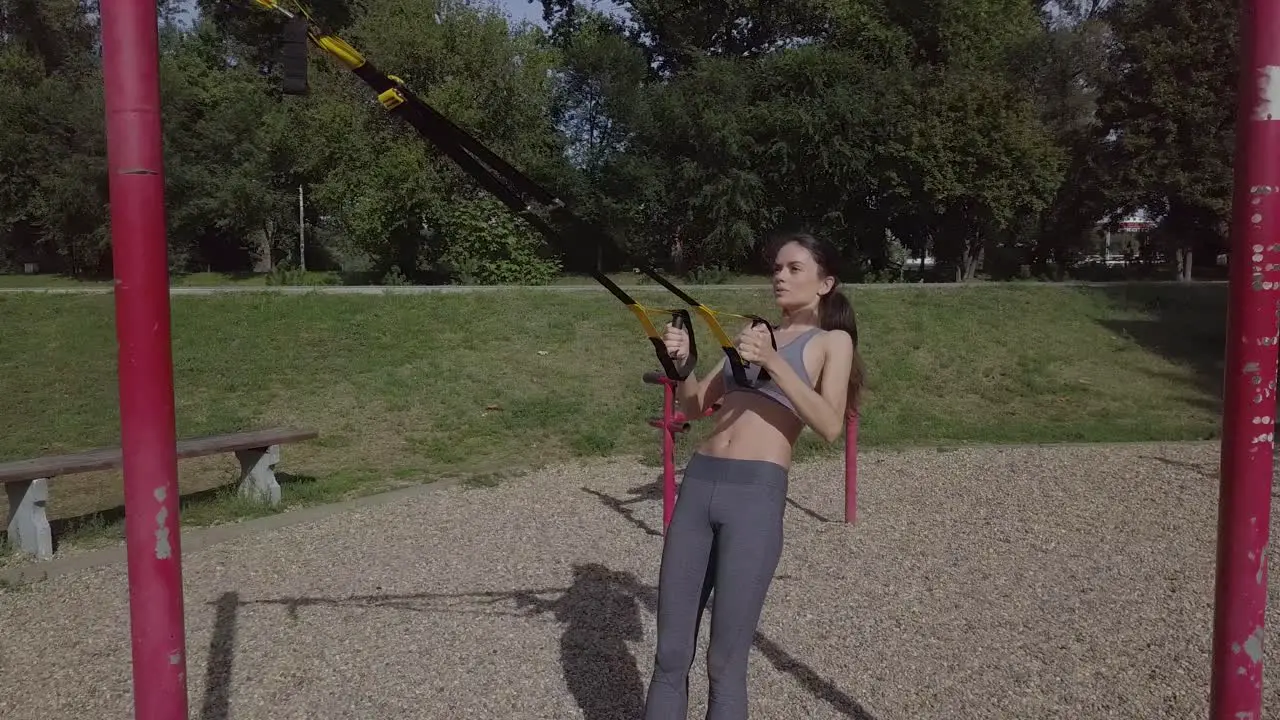 Young slim sporty girl doing TRX back workout sporty woman fitness outdoors