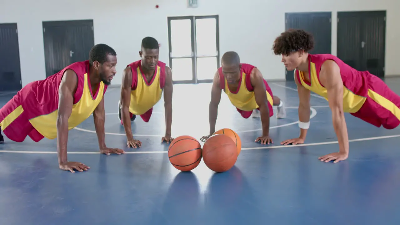 Diverse basketball players perform push-ups in a gym