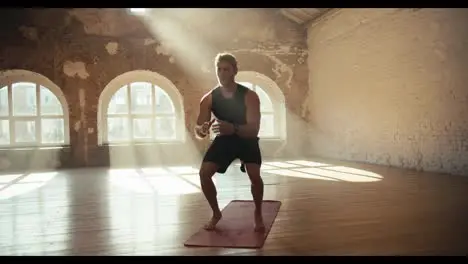 A man does exercises and squats in a sunny gym on a special carpet for sports Doing sports in the sunny gym workout in the morning