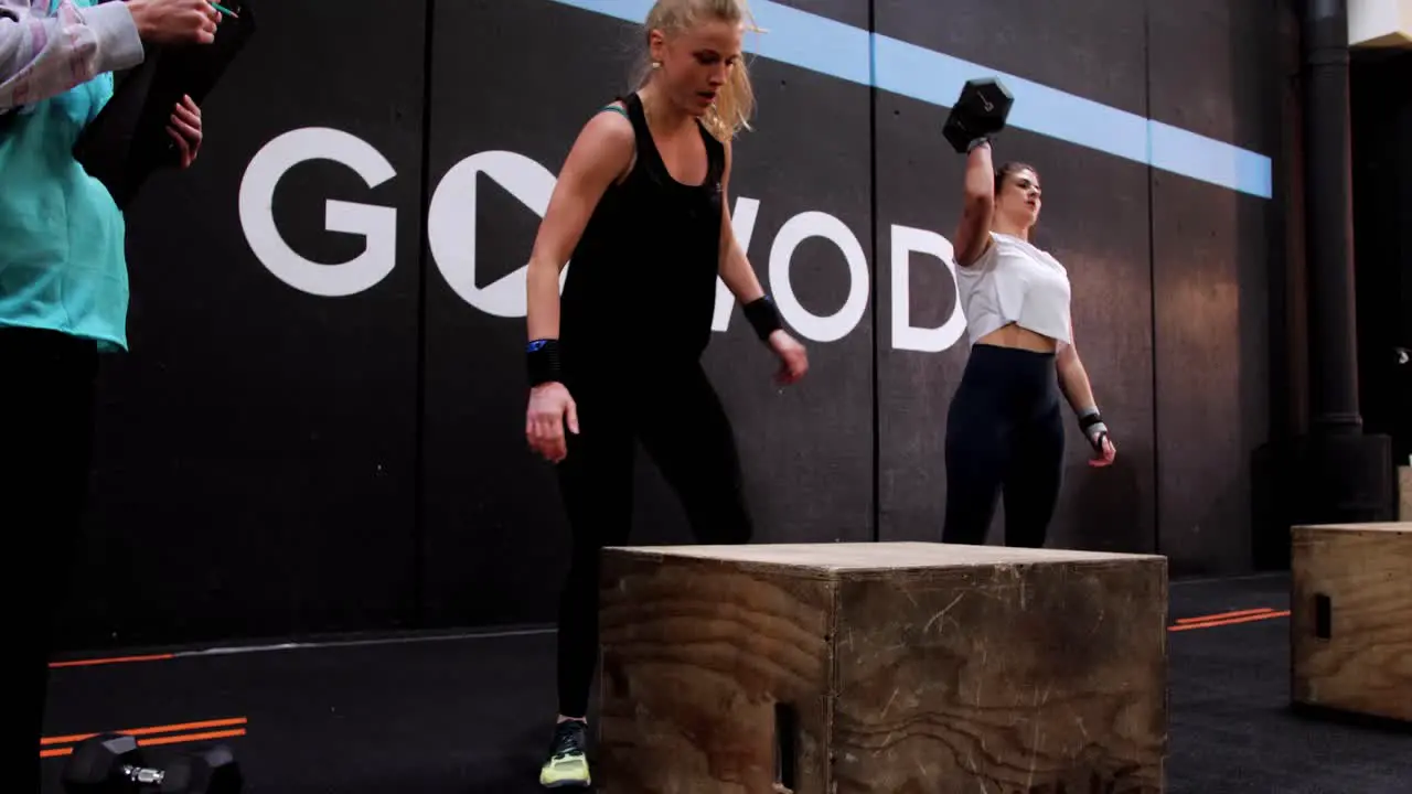 a young blonde Caucasian woman jumping on a wooden crate during a crossfit competition called "box jump"