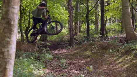 Slow Motion Shot Of Man On Mountain Bike Making Mid Air Jumps On Dirt Trail Through Woodland