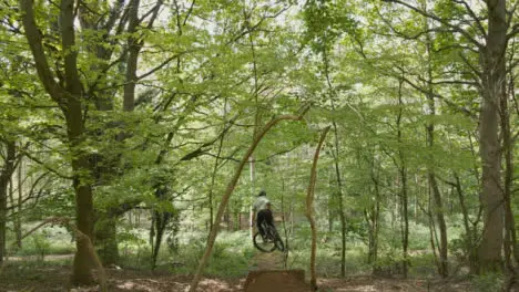 Drone Tracking Man On Mountain Bike Cycling Doing Mid-Air Jumps On Trail Through Countryside And Woodland