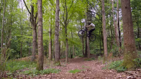 Slow Motion Shot Of Man On Mountain Bike Making Mid Air Jump On Dirt Trail Through Woodland