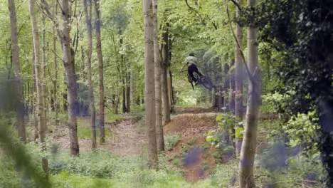 Slow Motion Shot Of Man On Mountain Bike Making Mid Air Jump On Dirt Trail Through Bluebell Woods