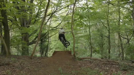 Drone Tracking Man On Mountain Bike Cycling Doing Mid-Air Jump On Trail Through Countryside And Woodland