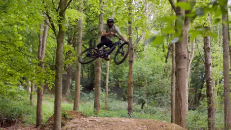 Slow Motion Shot Man On Mountain Bike Making Mid Air Jump On Dirt Trail Through Woodland 2