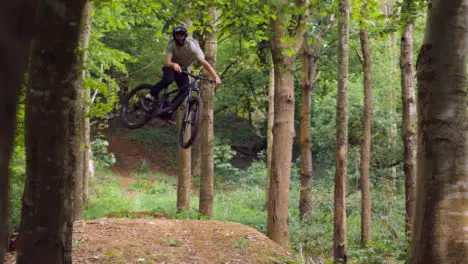 Slow Motion Shot Man On Mountain Bike Making Mid Air Jump On Dirt Trail Through Woodland