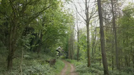 Drone Tracking Man On Mountain Bike Cycling Doing Mid-Air Jump On Trail Through Countryside And Woodland 2