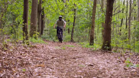 Slow Motion Shot Of Man On Mountain Bike Cycling And Doing Wheelie Along Trail Through Woodland 