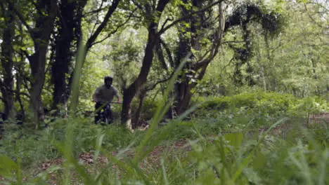 Low Angle Slow Motion Shot Of Man On Mountain Bike Cycling Along Trail Through Woodland