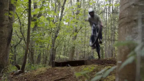 Man On Mountain Bike Making Mid Air Jump On Dirt Trail Through Woodland