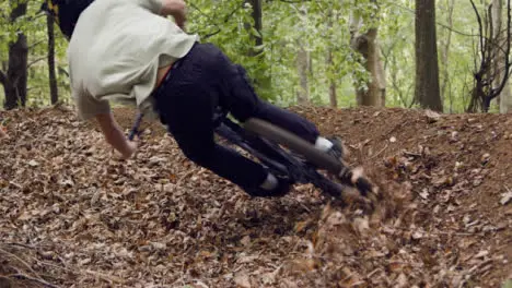 Low Angle Shot Of Man On Mountain Bike Cycling Along Dirt Trail Through Leaves In Woodland