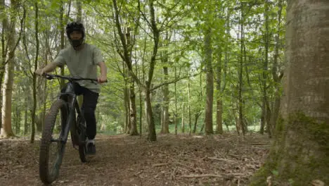 Drone Tracking Man On Mountain Bike Cycling Doing Wheelie Along Trail Through Countryside And Woodland