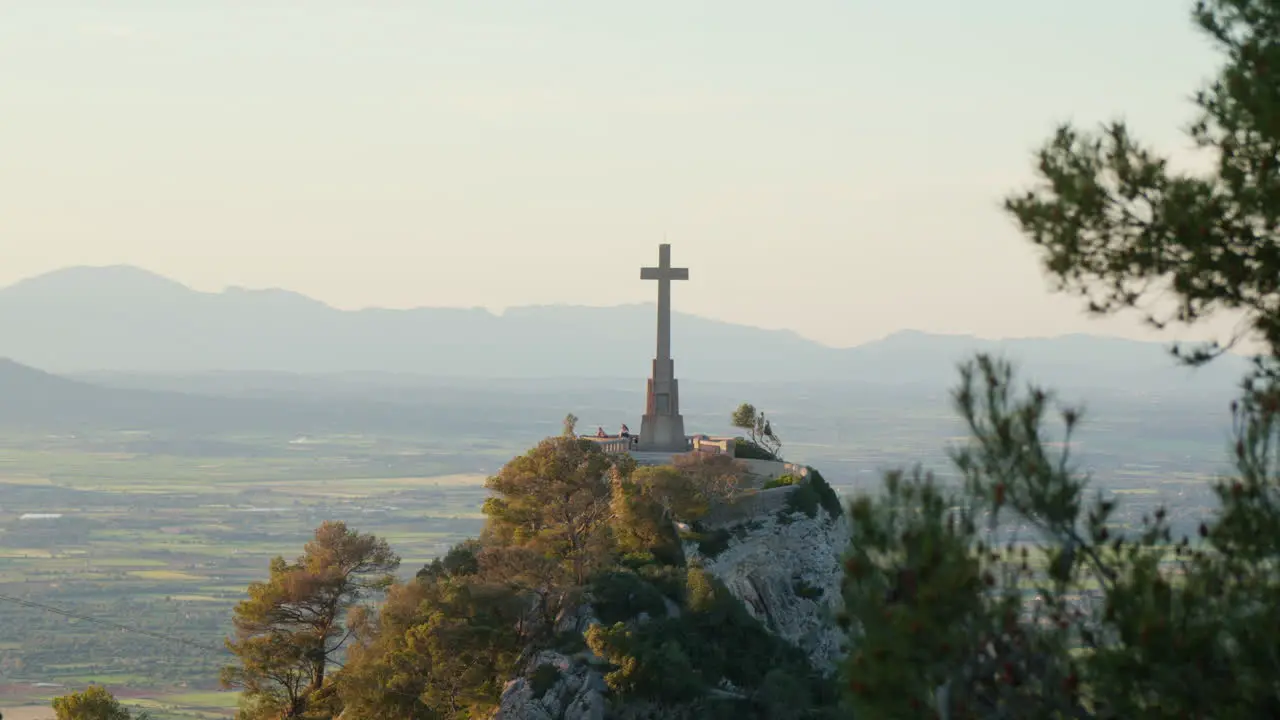 A hill at the Santuari de San Salvador in Mallorca Spain crowned by a cross with a mountain range forming a majestic backdrop in the late afternoon