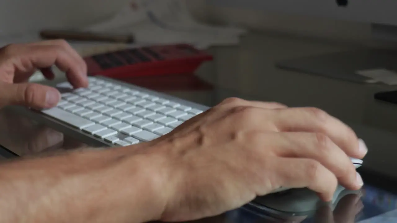 Male hands closeup typing on bluetooth keyboard and draging mouse over glass table