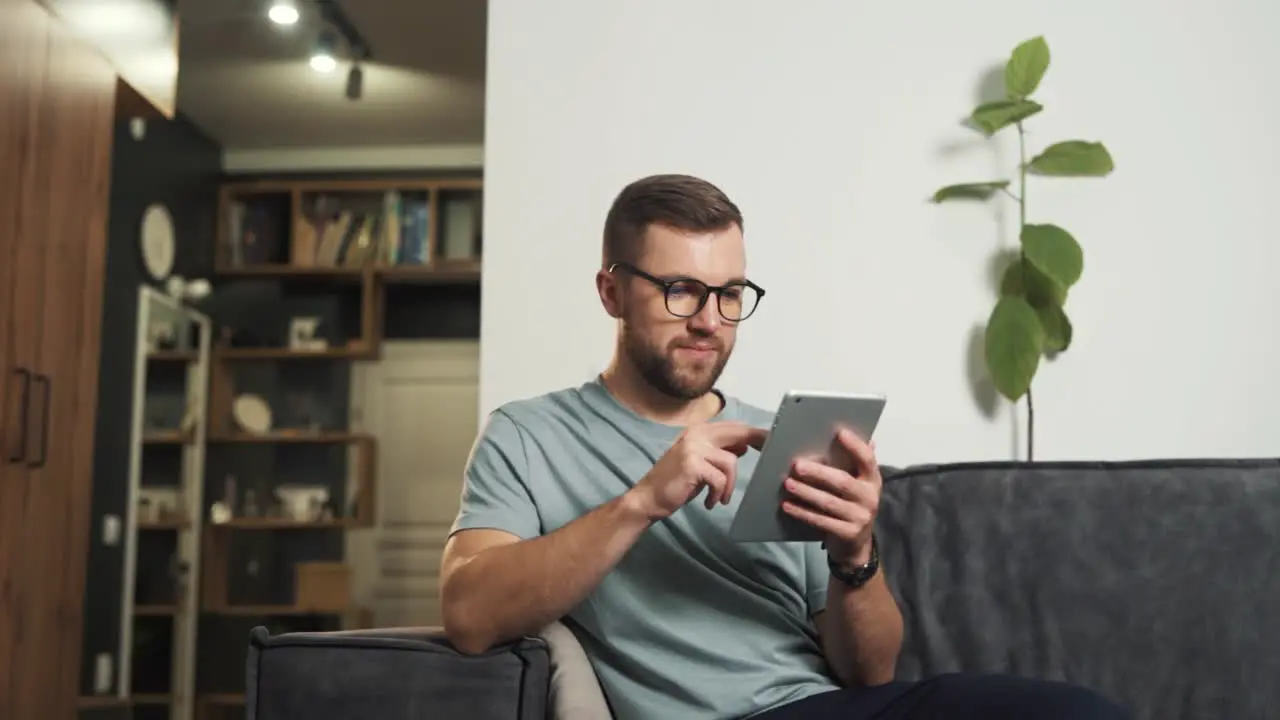 A handsome man in glasses searches the Internet through a tablet