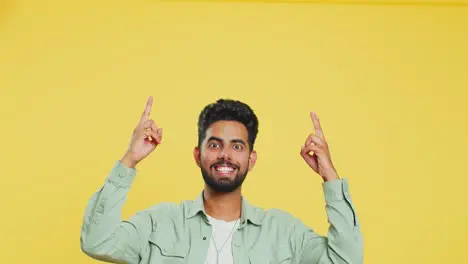 Young man showing thumbs up and pointing overhead on blank space place for your advertisement logo