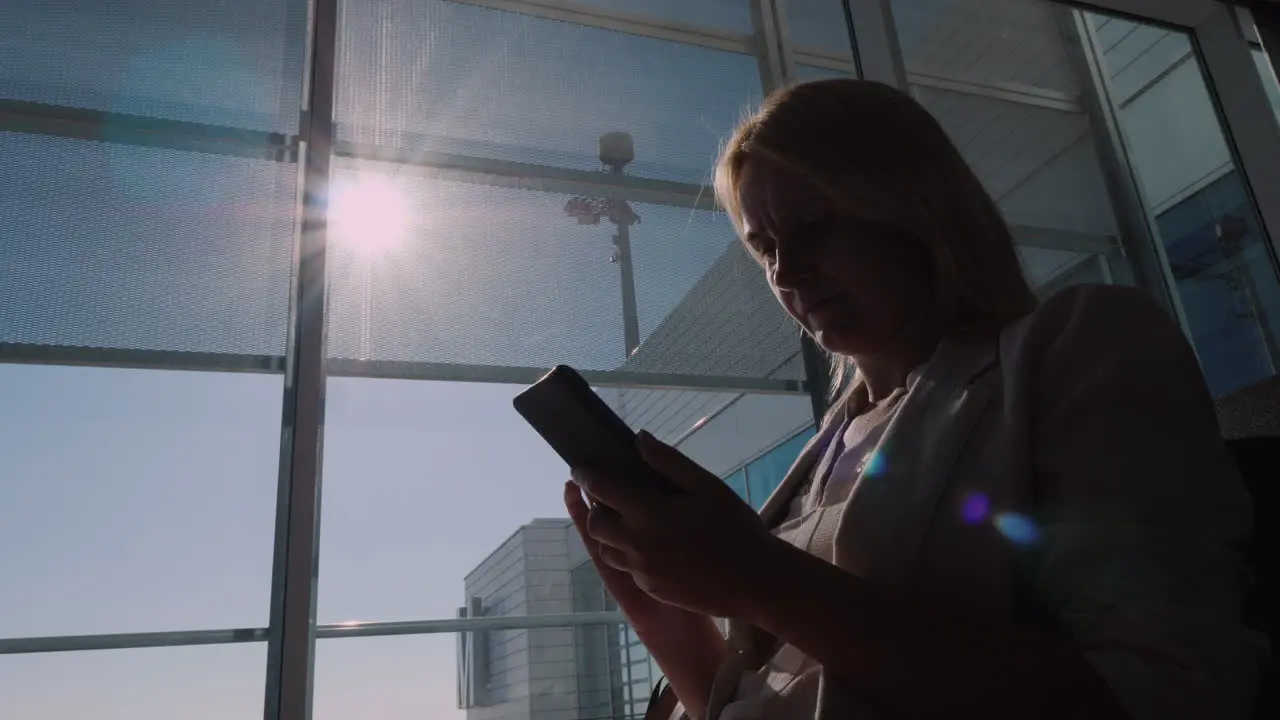 A Woman Is Waiting For Her Flight At The Airport Terminal Using A Smartphone