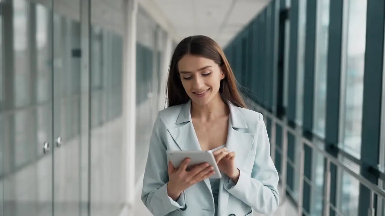 Stylish young beautiful woman in a suit walking down the hall with a tablet