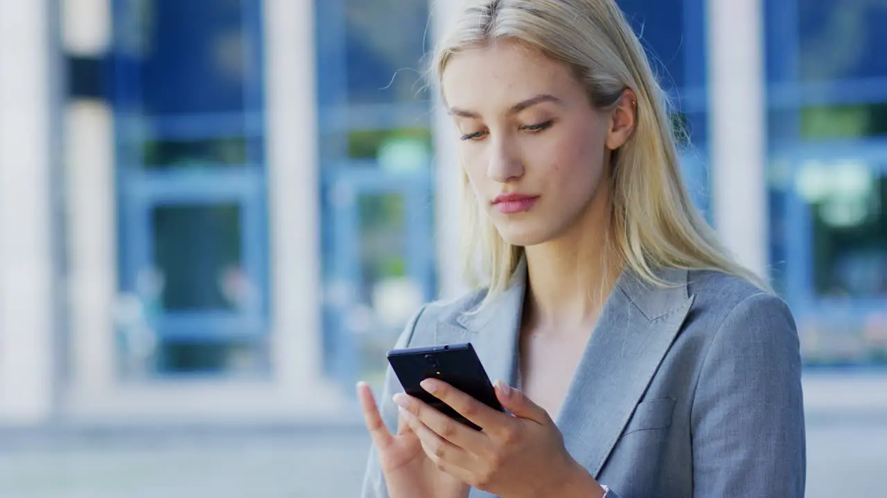 Young businesswoman using smartphone near building