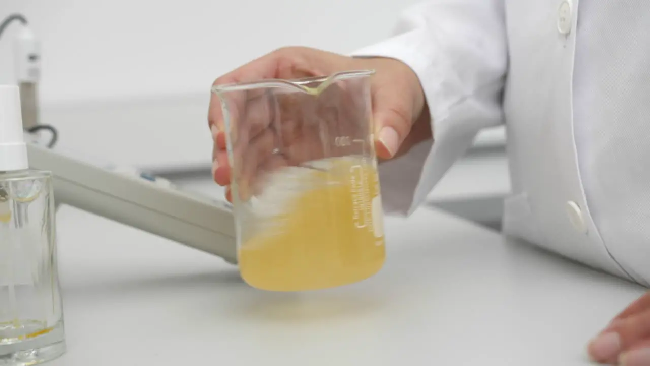 closeup of female scientist mixing yellow liquid in beaker in scientific lab slow motion