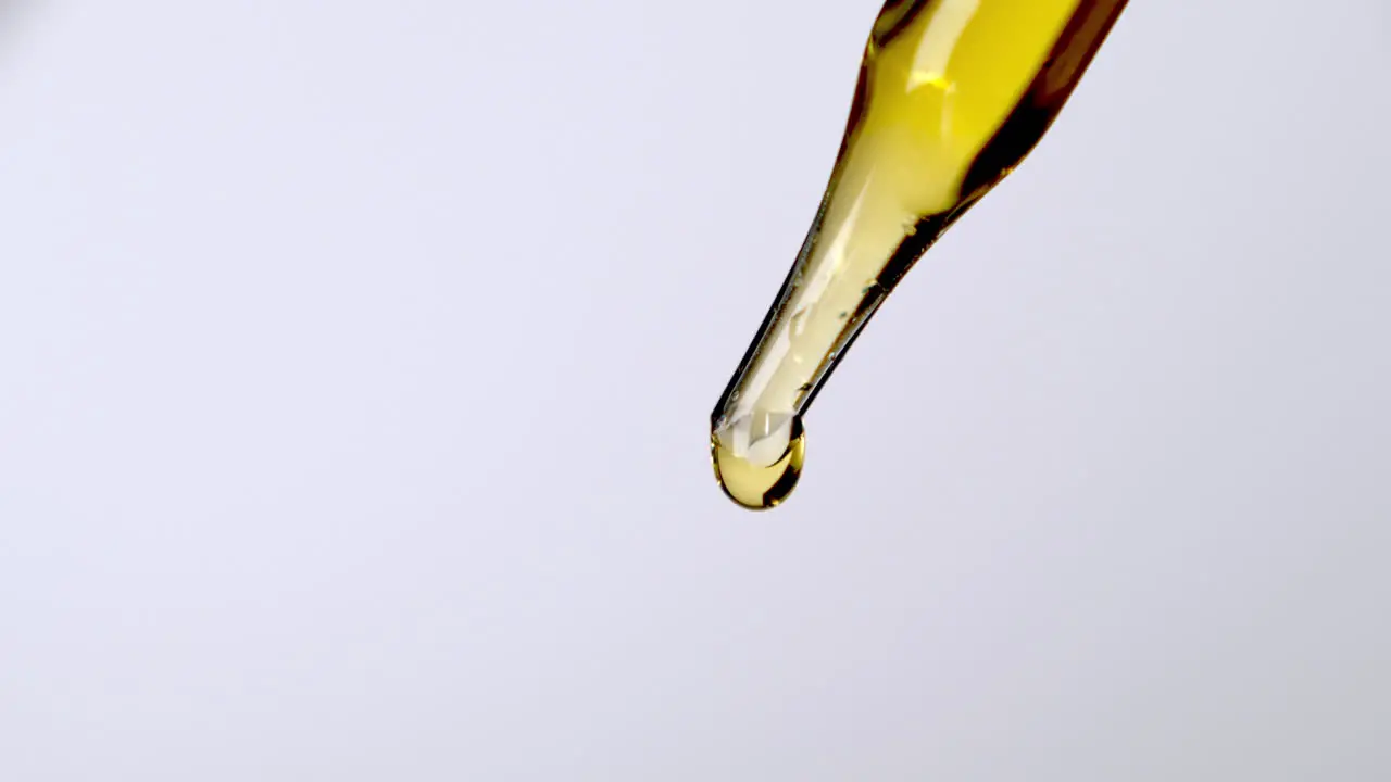 Yellow liquid drops falling from glass pipette close up view isolated on white background