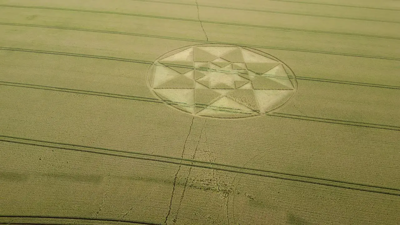 Rising aerial view to reveal symmetrical star crop circle pattern on golden Hampshire wheat field 2023