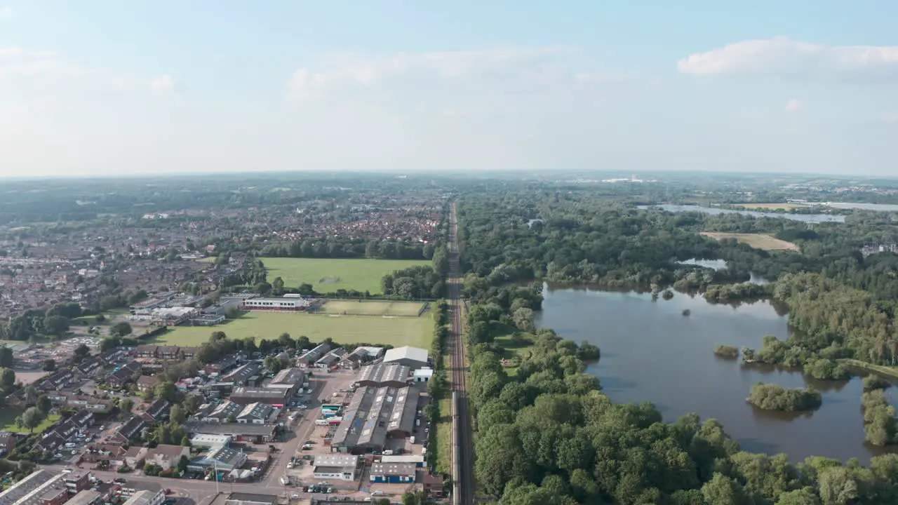 Follow drone shot over British rail train along long straight track in the countryside