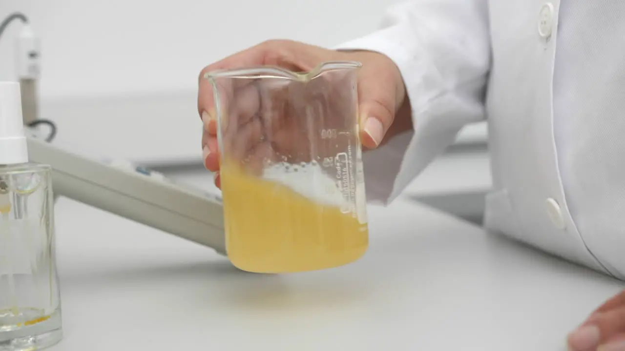 detail of scientist stirring yellow liquid in beaker natural light indoor