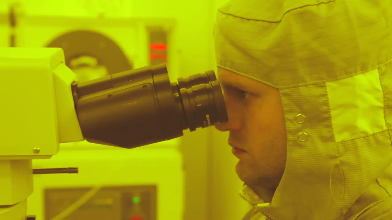 Close shot of male researcher in full medical suit working in laboratory looking through microscope