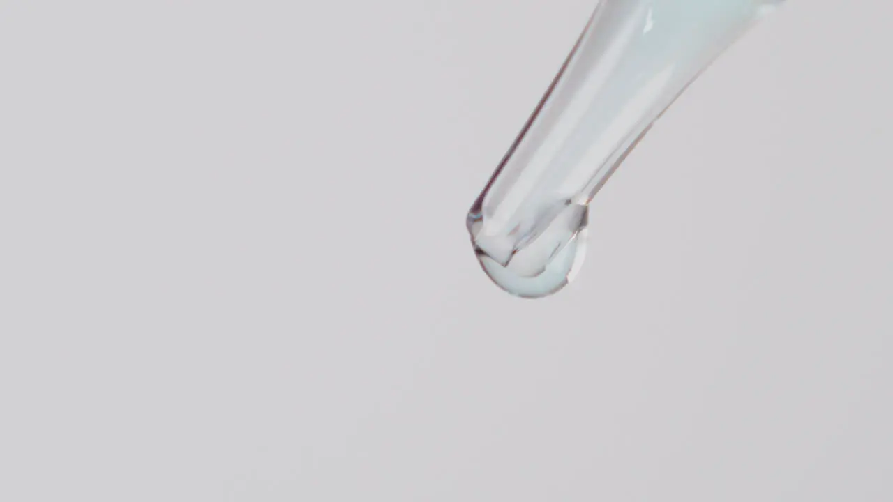 Close up of transparent liquid droplets slowly falling on white background