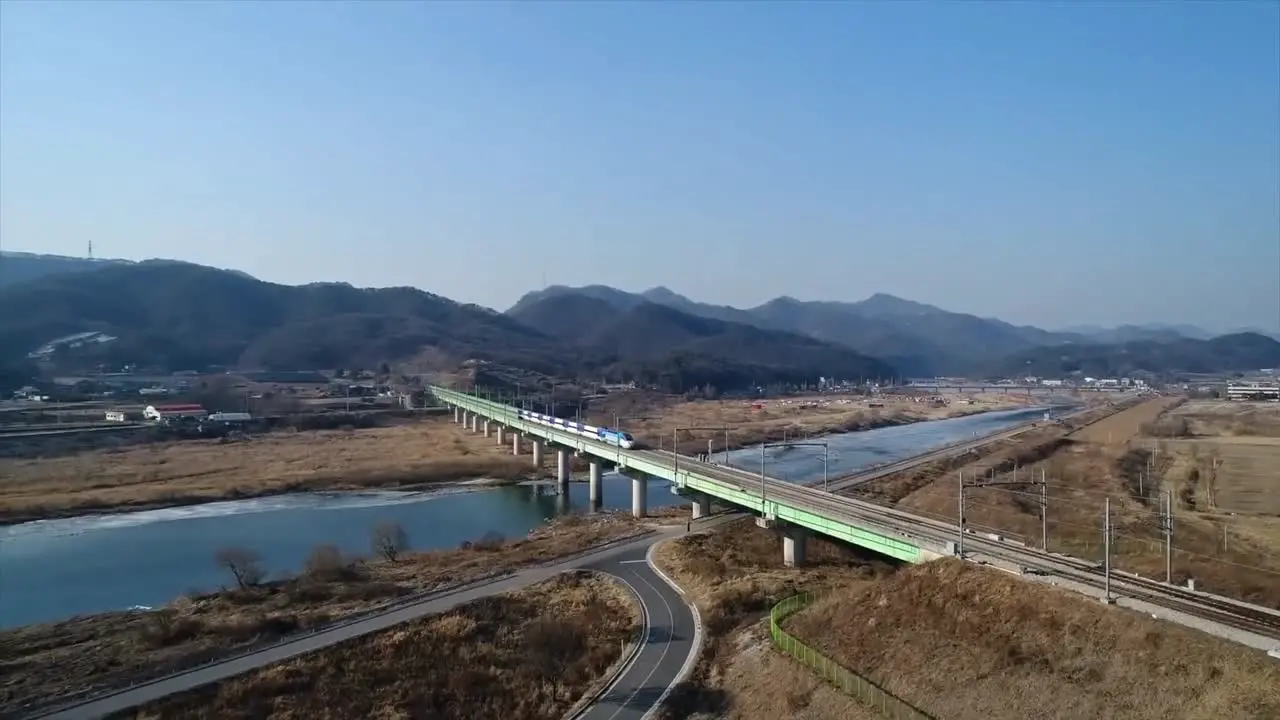 High speed train passing from a bridge over a river with blue water and mountains in the background