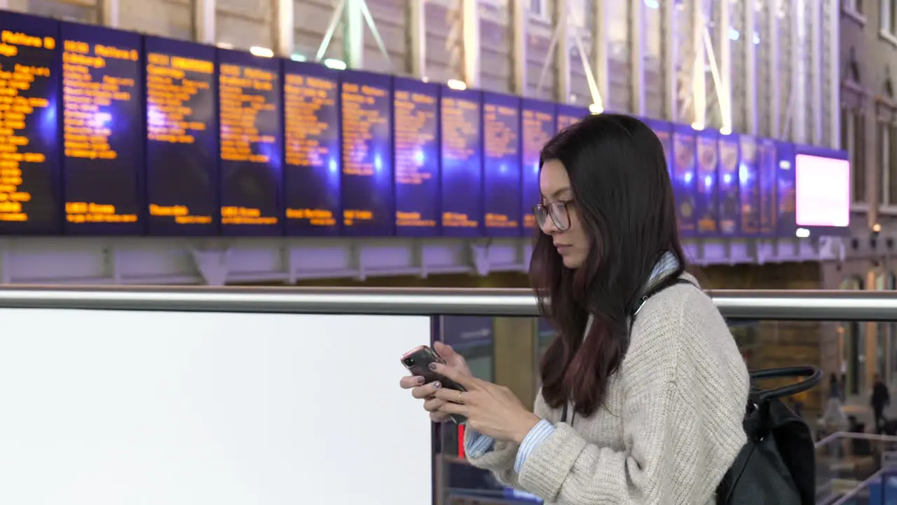 Young student tourist checks her phone while waiting for a train at Kings Cross Station London England