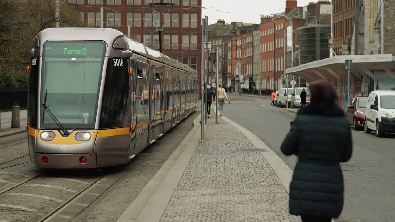 Woman walking away from camera as public train approaches in Dublin Ireland