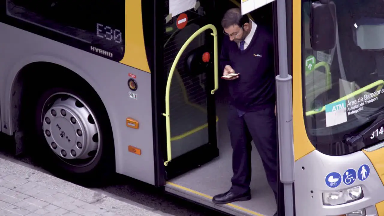 COVID-19 handheld close up of a driver-conductor checking his mobile standing at the empty bus door