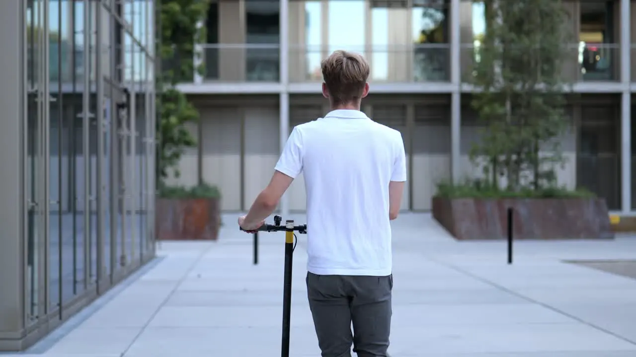 Back view of a young businessman walking with an e-scooter medium shot