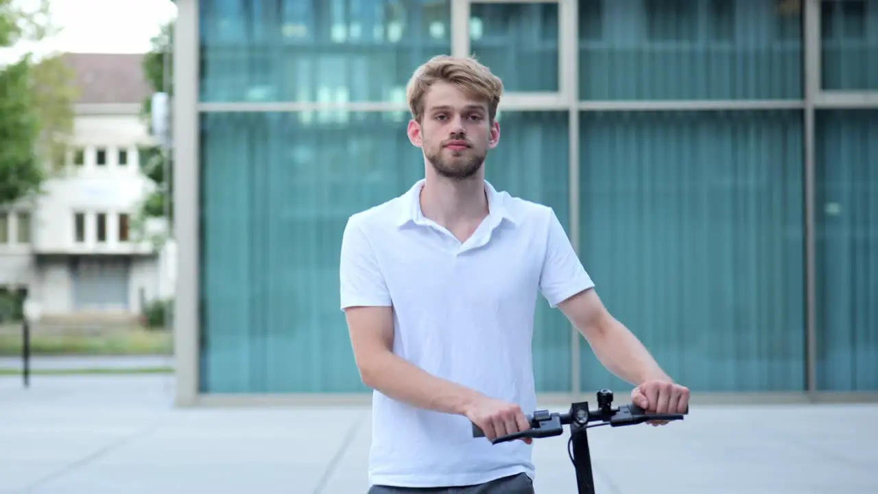 A young businessman walks past a modern building on an e-scooter