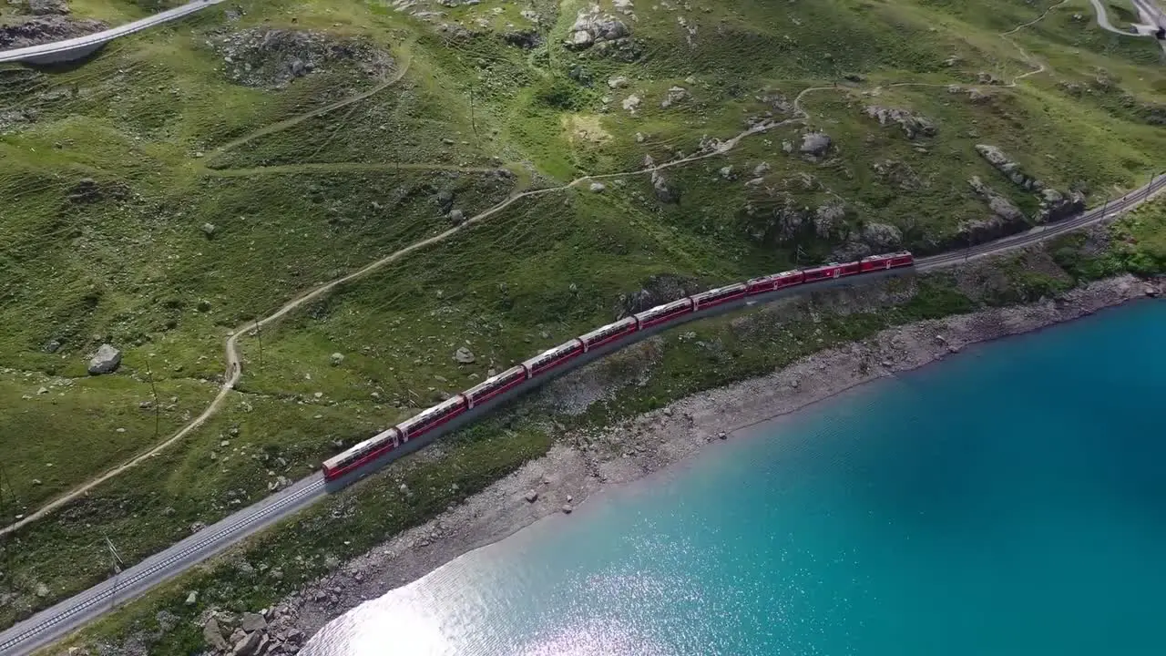 Aerial clip showing a train moving along the green hills adjutant to a lake with blue water