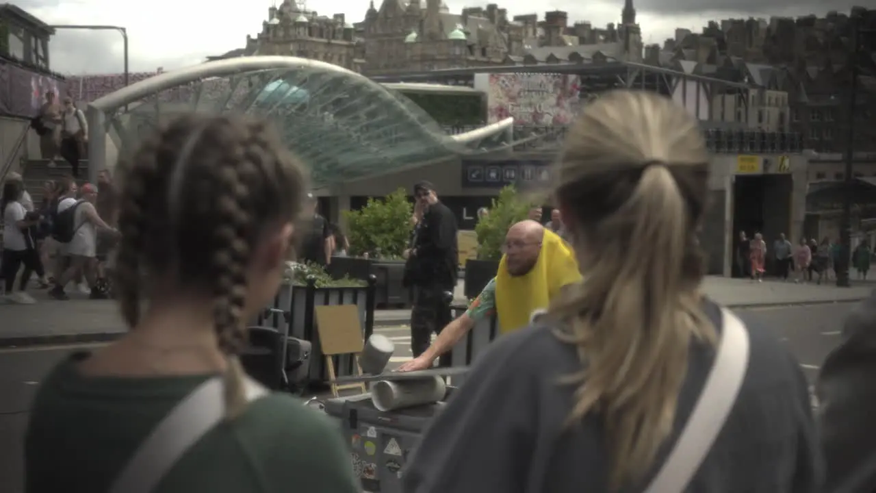 Witness an extraordinary man performing a captivating balancing act and then stepping down in the vibrant city of Edinburgh captivating a crowd as two girls watch in the foreground