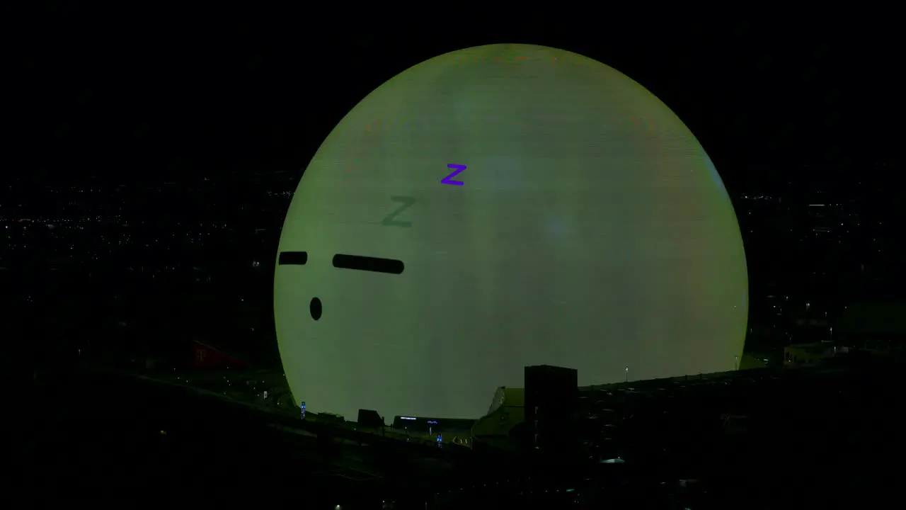 Illuminated MSG Sphere With Sleeping Emoji Face And Waking Up On Surface Looking Around At Night