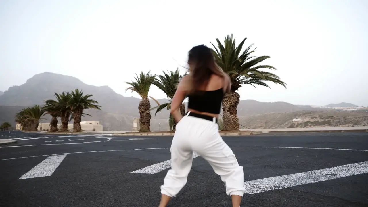 Girl In White Is Dancing Outdoor At The Road With Tropical Trees And Hills On Background