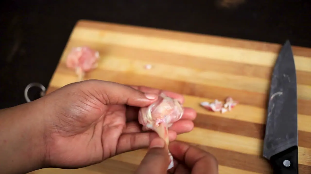 chef cutting raw chicken wings with a sharp knife and shaping into a lollipop on a cutting board