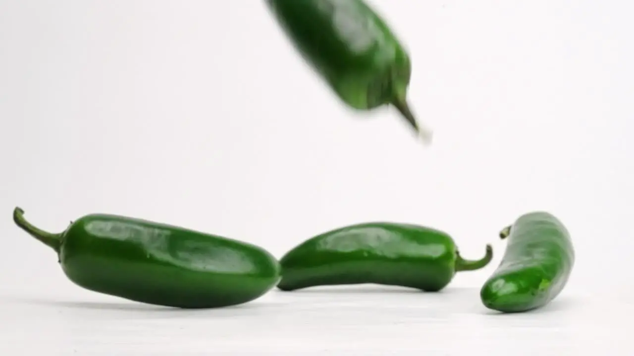 Whole green jalapeños falling and bouncing on white studio backdrop in 4k slow motion