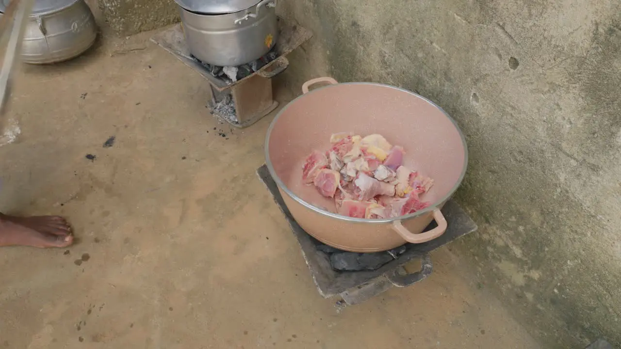 black female African woman preparing meat in a pot in outdoor kitchen in rural remote village of ghana