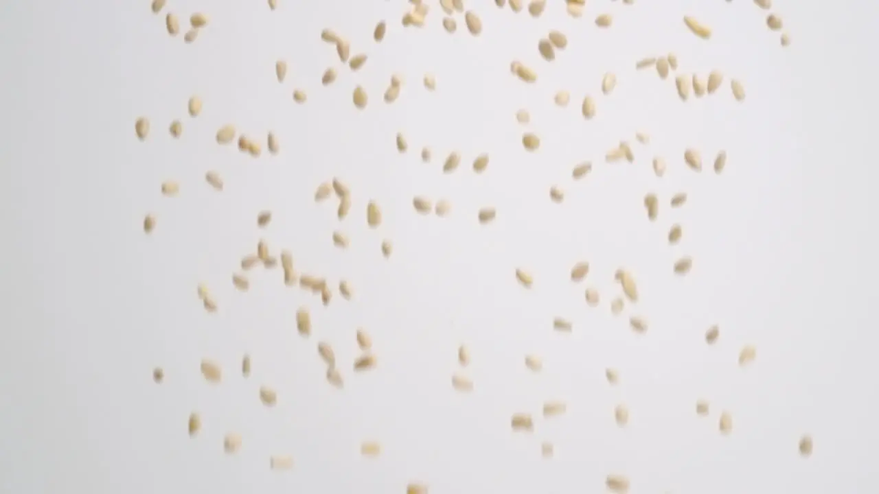 Small pine nuts raining down on white backdrop in slow motion